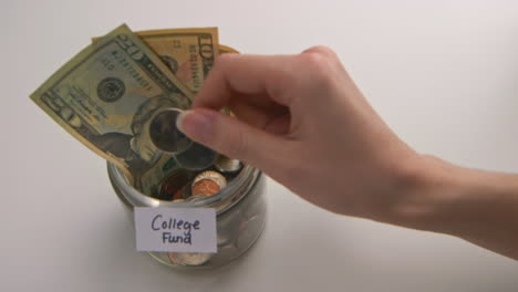 a caucasian woman's hand puts two american quarters into a &quot;college fund&quot; jar