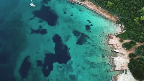 Slow-motion-drone-shot-over-a-sailboat-in-the-sea-with-light-blue-color-and-the-sea-floor-with-darker-blue-spots