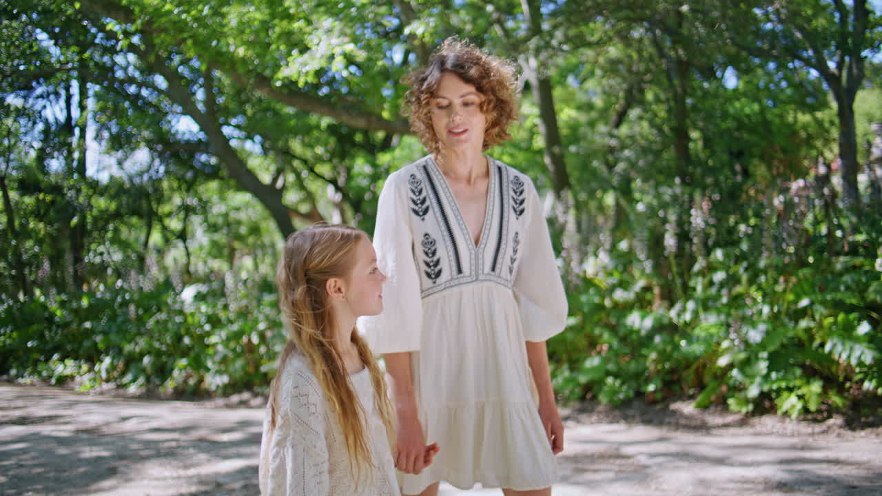 Happy mother walking daughter sunny garden alley at family weekend. Family love