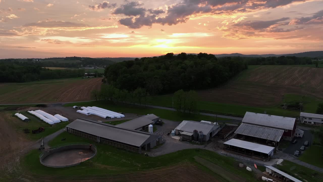 Dusk scene in american rural district with farmstead and barn at sunset time. Aerial wide shot. Forest landscape and agricultural farm fields in midwest of america.