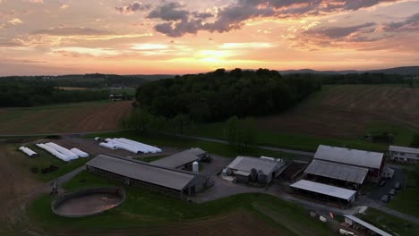 dusk scene in american rural district with farmstead and barn at sunset time. aerial wide shot. forest landscape and agricultural farm fields in midwest of america.