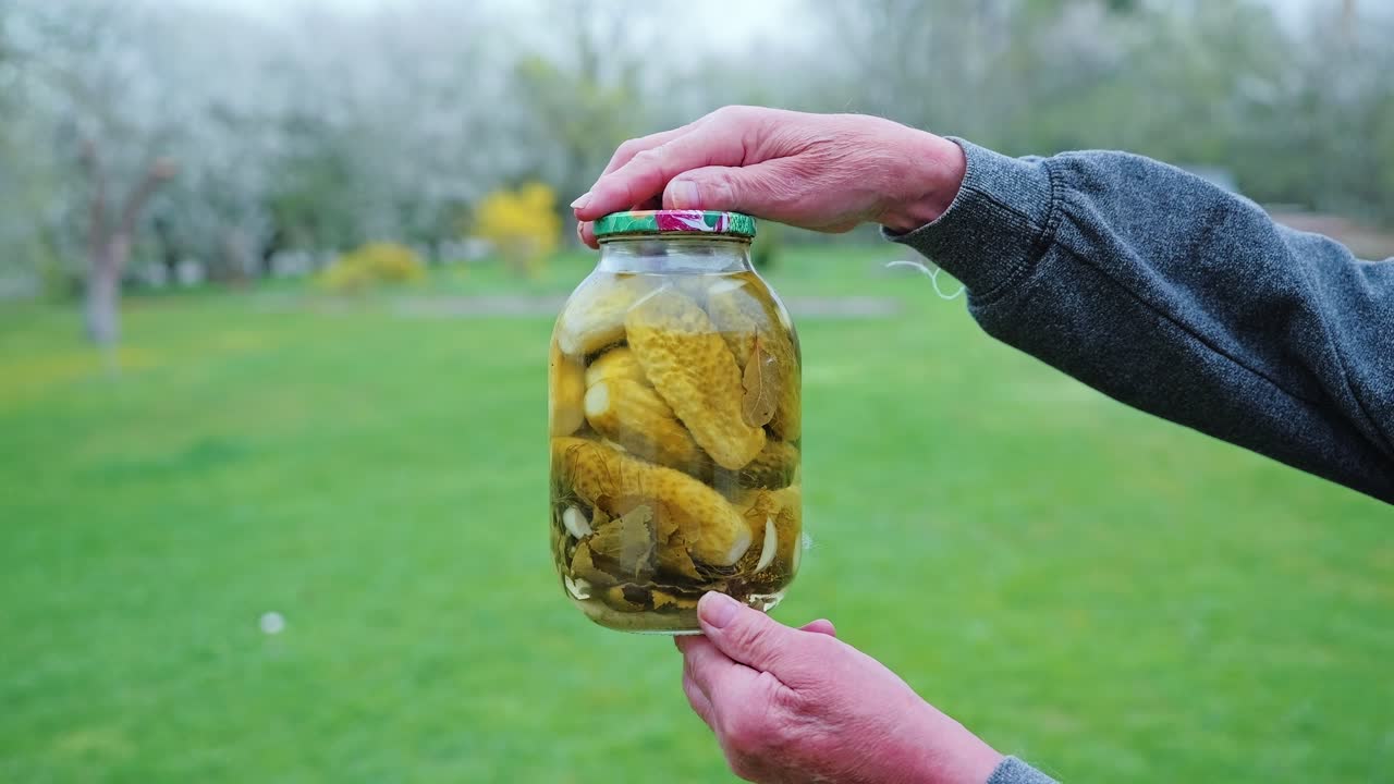 Slow motion, elder lifting pickle jar on green grass in Latvian countryside, 4K