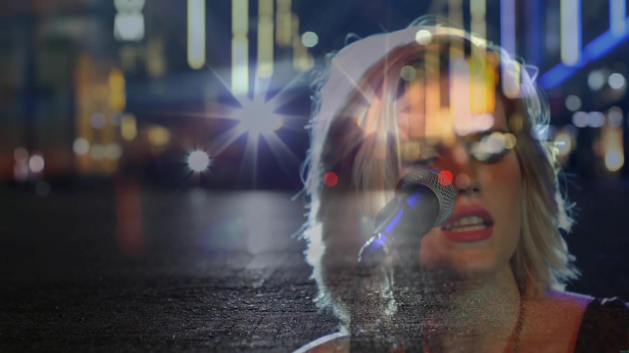 Oncoming headlights starting double exposure as female artist strumming guitar and singing into mic