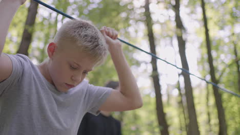 los niños en una caminata de campamento de verano se mueven a lo largo de las cuerdas con la ayuda de un guía que enseña a los niños escalada en roca y turismo. un niño en el bosque supera una barrera de cuerda