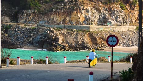 Surfer-Fährt-Auf-Der-Küstenstraße-In-Vietnam-Mit-Dem-Motorrad-Mit-Gelber-Tafel-Auf-Dem-Gepäckträger