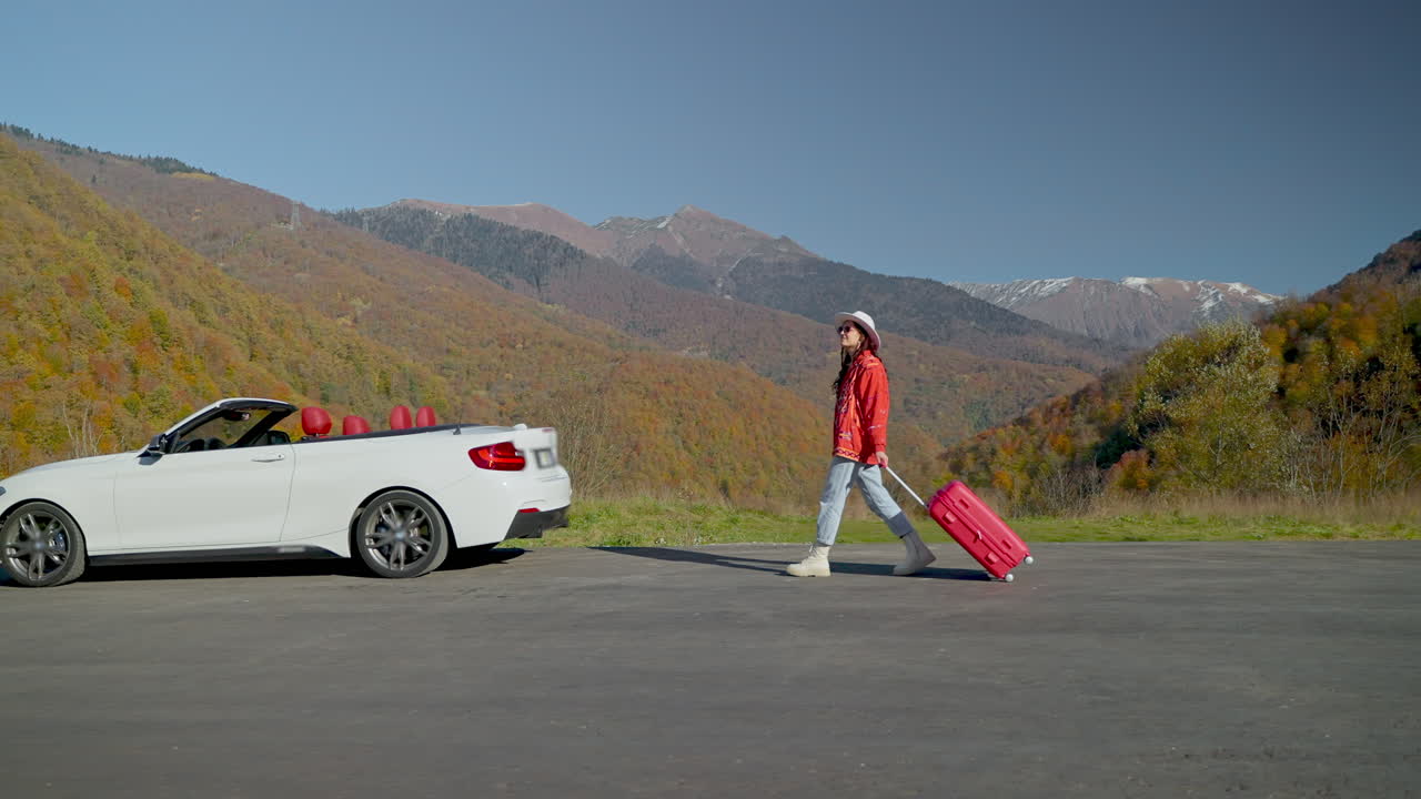 가을의 산에서 색 컨버터블 자동차 근처에 빨간 가방을 가진 여자
