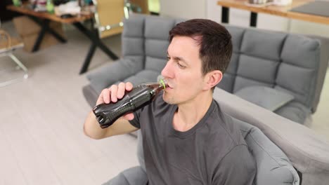 man drinking from a bottle while sitting on a sofa