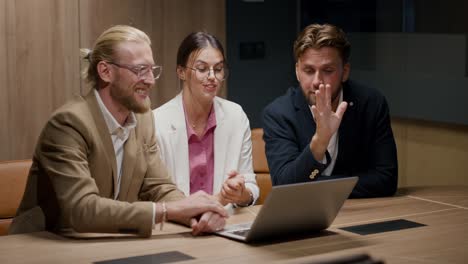 two guys in business suits and a girl in a business suit are sitting in front of a laptop and holding a video conference with their employees. online conference for communication and solving your problems