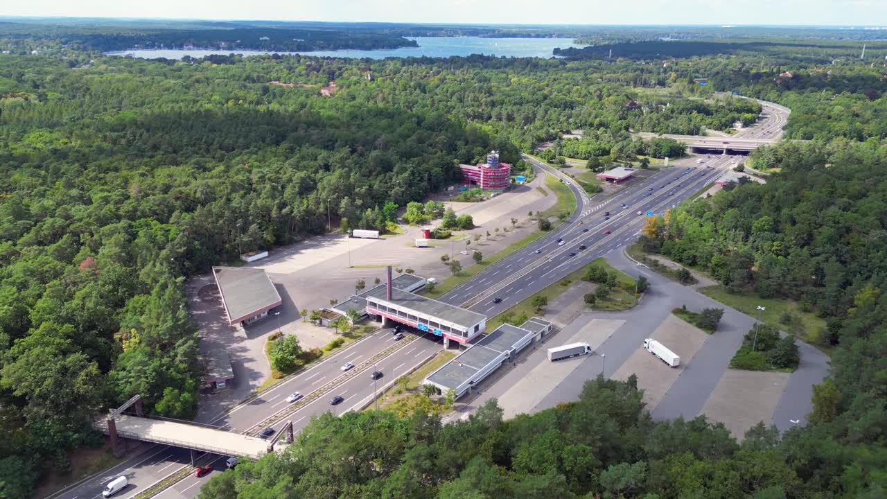 Cars driving on a freeway interchange surrounded by forest leading to a lake on a cloudy day. Stunning aerial view flight ascending drone