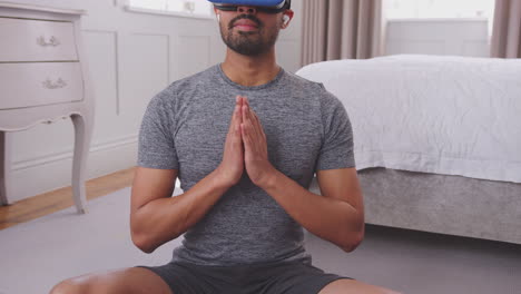 Mann-Sitzt-Zu-Hause-Auf-Einer-Yogamatte-Im-Schlafzimmer,-Trägt-Ein-Virtual-Reality-Headset-Und-Drahtlose-Kopfhörer-Und-Streamt-Virtuelle-Kurse-Vom-Mobiltelefon-Aus-–-Aufgenommen-In-Zeitlupe