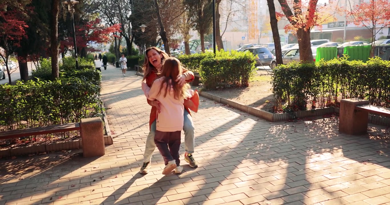 Hija feliz corre hacia su madre en un parque de la ciudad en un día soleado