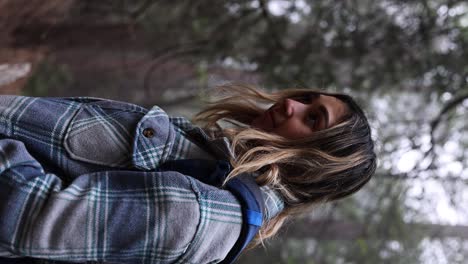 attractive latina hiker in a blue checkered flannel looking up into some fog-covered trees vertical