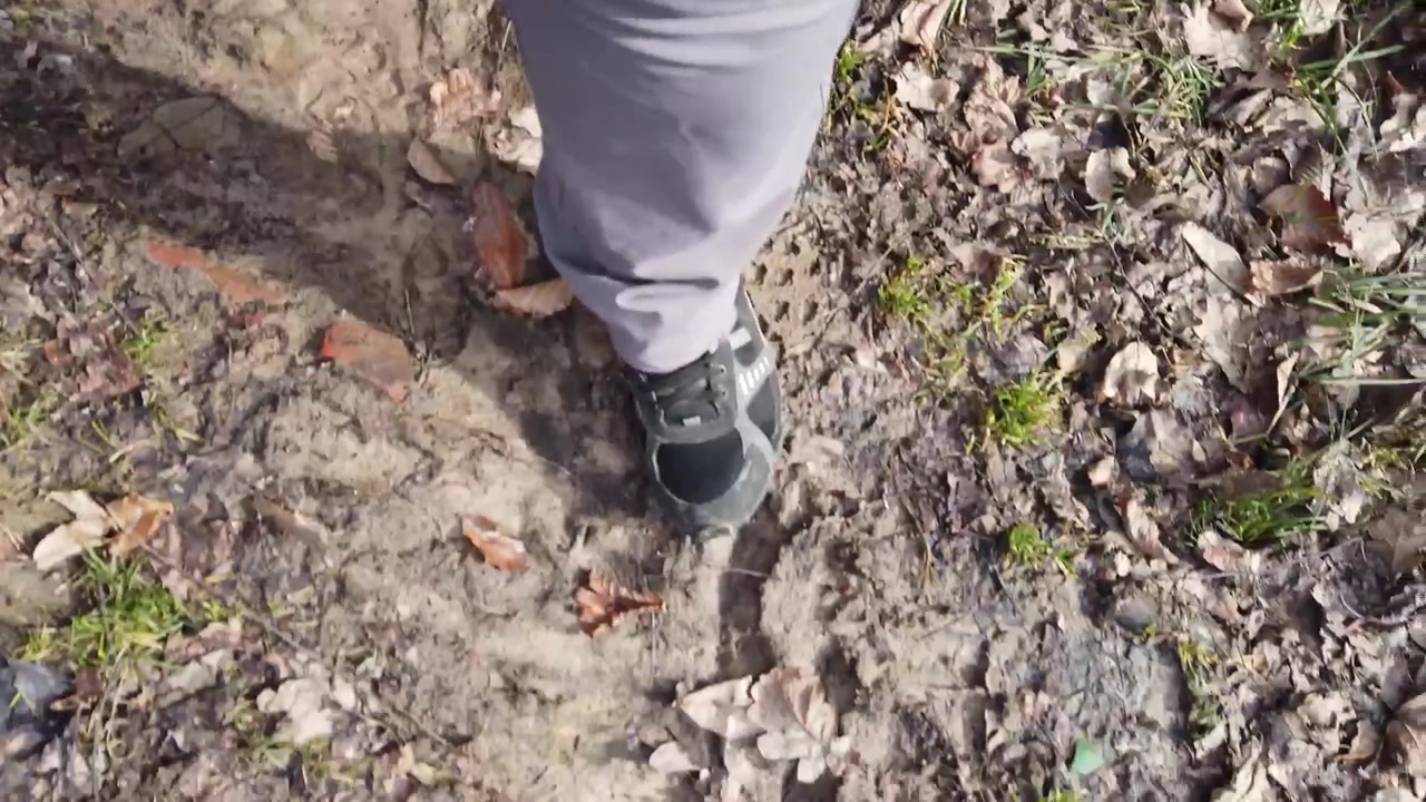A woman in sneakers walks down a forest road.