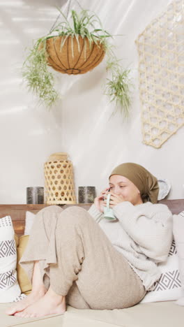 video shows biracial woman in hijab, laughing, having coffee and chatting on phone at home