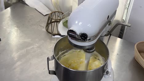 mano sosteniendo un tazón de huevos, vertiendo lentamente y agregando a las mezclas de pasteles, mezclando en el mezclador de la máquina