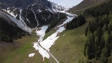 Aerial view of springtime in Austrian Alps where snow still lingers on the slopes as meltwater flows through green meadows
