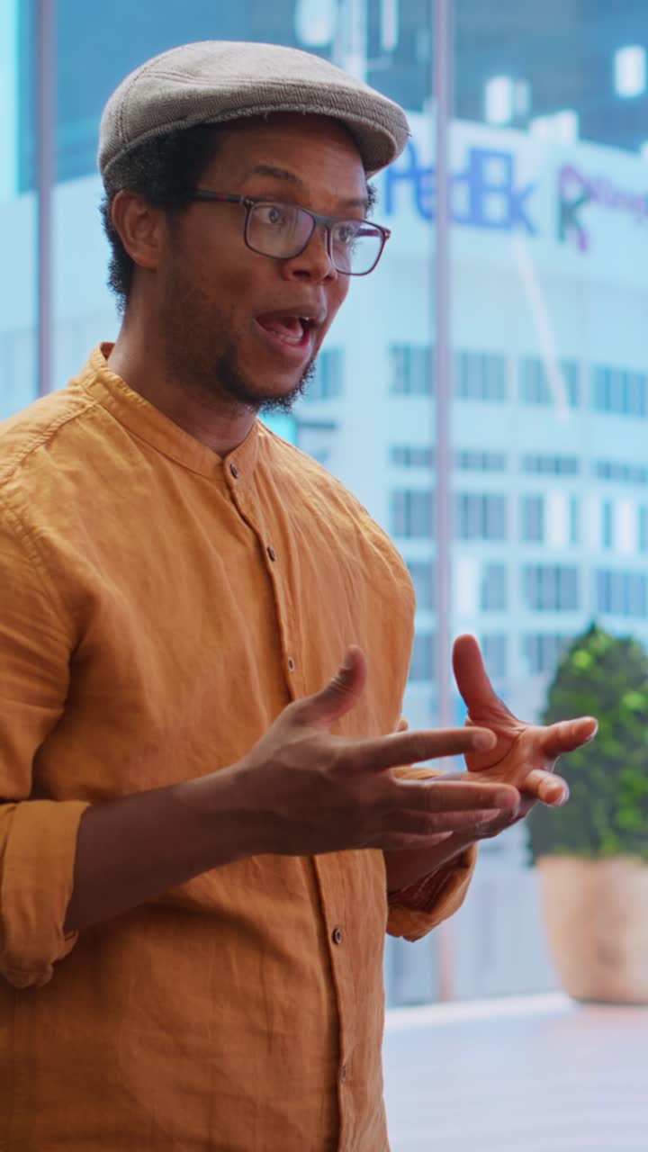 Man in Glasses and Flat Cap Talking and Gesturing in Modern Office