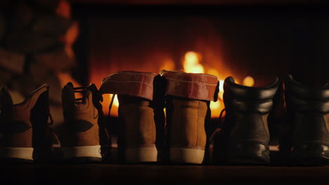 a few pairs of winter shoes are drying near the fireplace where the fire is on