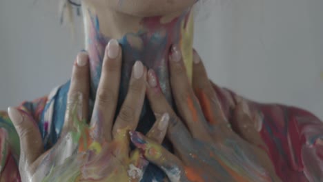 manos de mujer moviéndose hacia abajo desde su cuello mezclando pintura fresca y colorida sobre su cuerpo