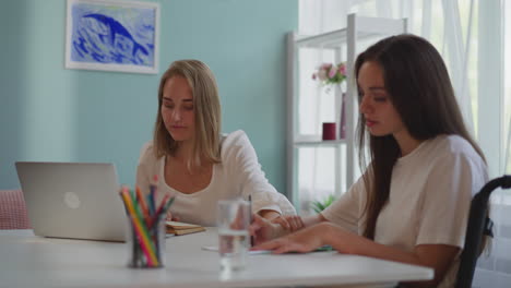 Young-woman-touches-hand-of-girl-partner-at-doing-homework