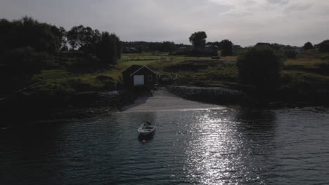 fishing boat at the seashore with cottage on countryside at dusk in nordland, norway. - aerial