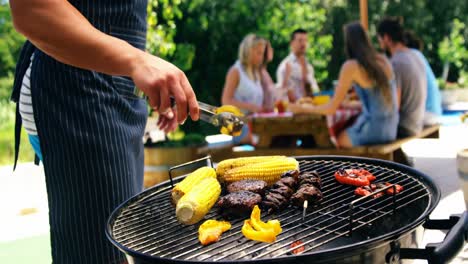 mid section of man grilling corn, meat and vegetable on barbecue