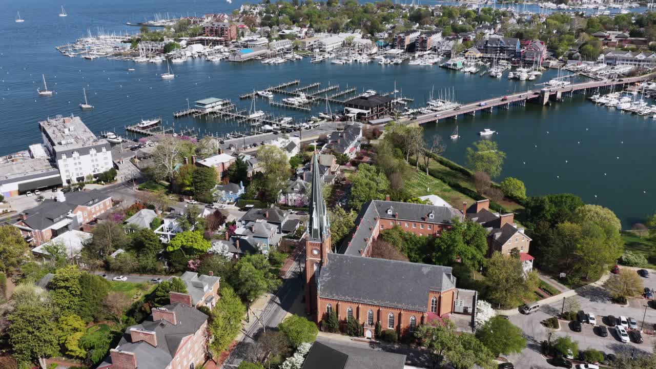 Vista aérea de Annapolis, Maryland, EUA, com campanário de igreja, marina e ponte à beira-mar, cercada por casas históricas e barcos sob a luz solar intensa da primavera ao longo da cênica Baía de Chesapeake. Plano amplo