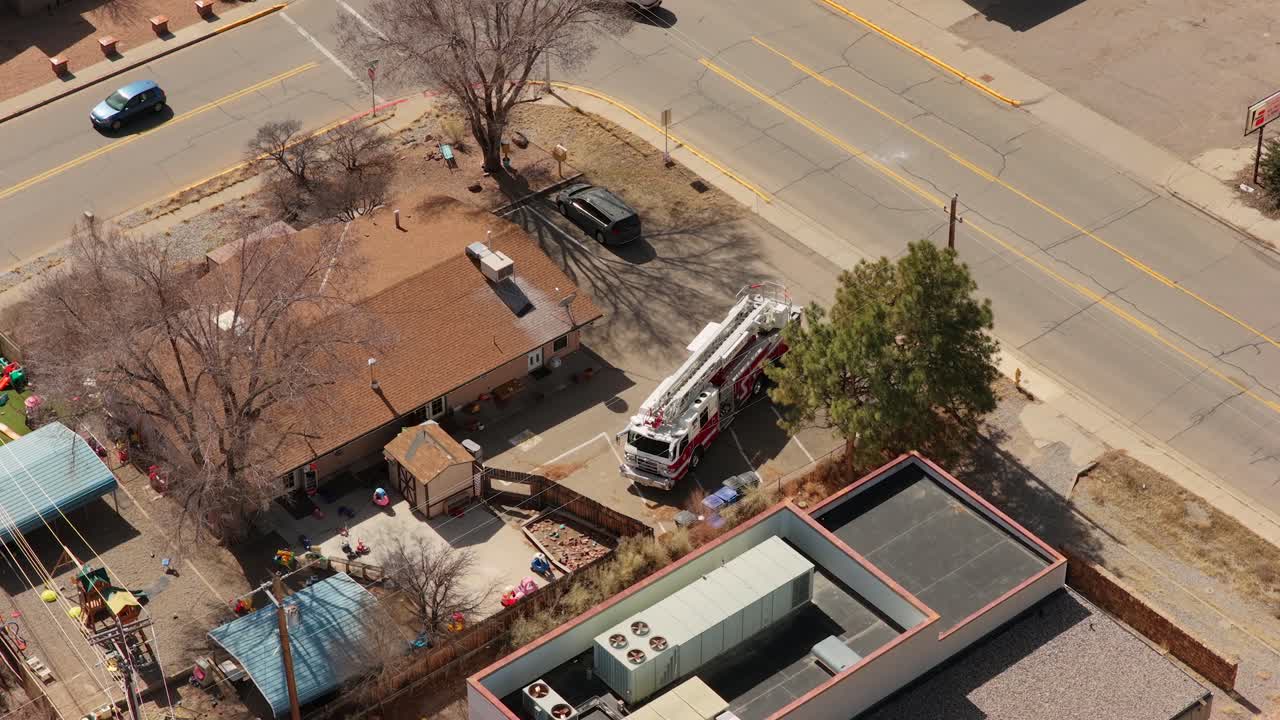 A high angle drone shot captures a red fire engine pulling into a parking lot. First responders begin to exit the vehicle in a professional community response scene in New Mexico