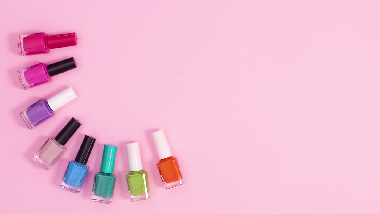 las botellas de esmalte de uñas de manicura se mueven en el lado izquierdo del fondo rosa pastel.