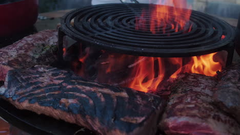big pieces of meat grilling on a barbecue with hot flames during the day, medium shot