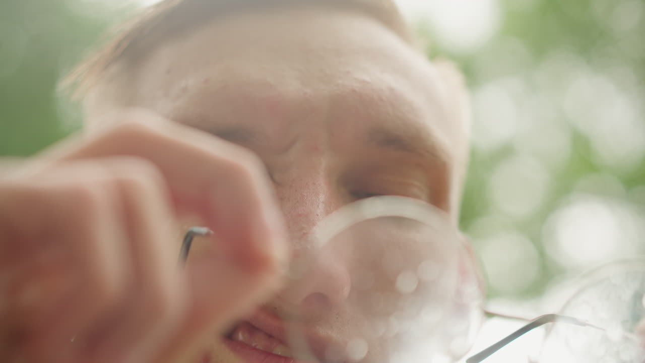 Young man cleaning, Caucasian person wiping glasses, Gentle sunlight illuminates young man cleaning wet spectacles, Wistful young man with raindropped glasses under soft summer sunlight