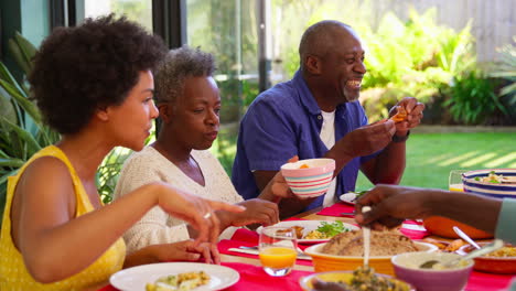 Padres-Con-Hijos-Adultos-Sentados-Alrededor-De-Una-Mesa-En-Casa-Disfrutando-De-Una-Comida-Juntos