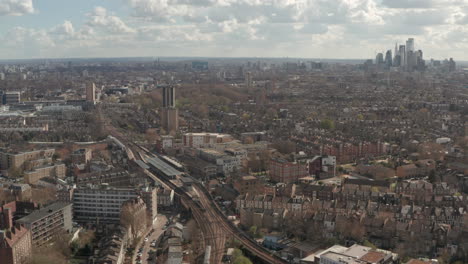 Descending-aerial-shot-of-London-skyscrapers-while-train-arrives-at-Hackney-downs-station