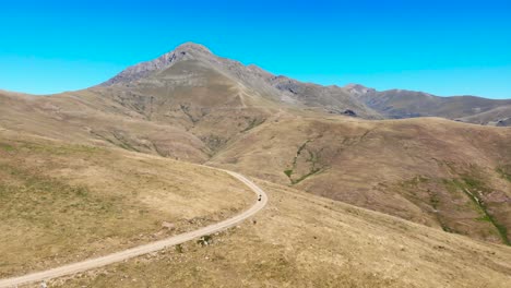 Aerial:-mountain-biker-going-uphill-in-a-high-mountain-deserted-area-in-summer-time-under-a-blue-sky