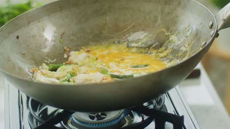 mujer añadiendo fideos de arroz a los ingredientes en la sartén