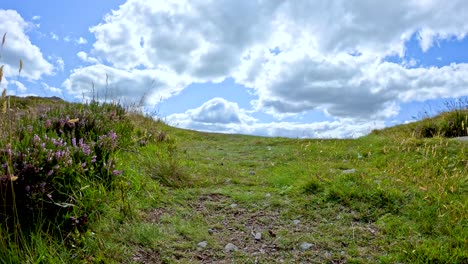 A steady walk up a narrow, grassy hill path in Glen Clova, Angus, Scotland, under bright daylight with dynamic clouds and wide landscape views