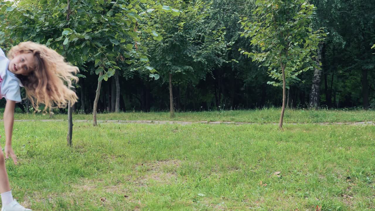 Happy baby girl jumping, dancing on the grass in the summer park. Cartwheel jump