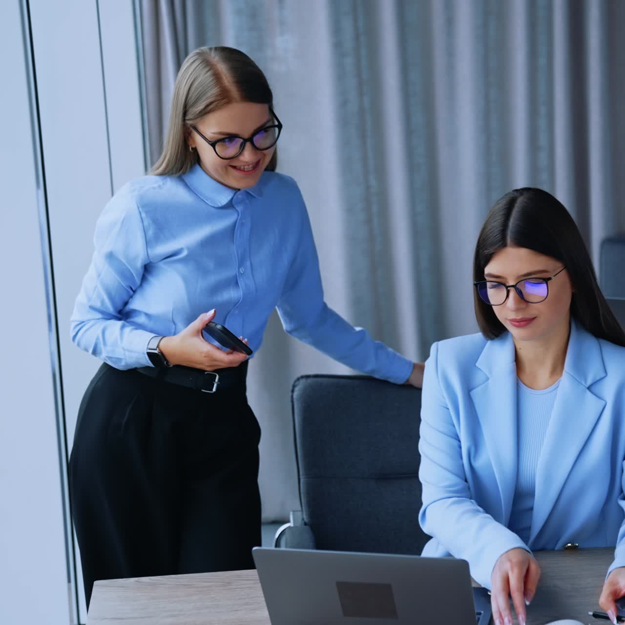 Ladies working together in office discussing job issues. Female co-workers look at laptop and taking notes. Office backdrop
