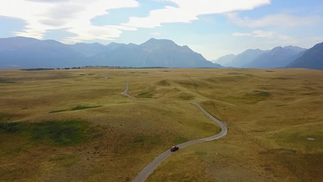 Aerial-tracks-car-on-twisty-road-on-hilly-moraine-in-mountain-valley