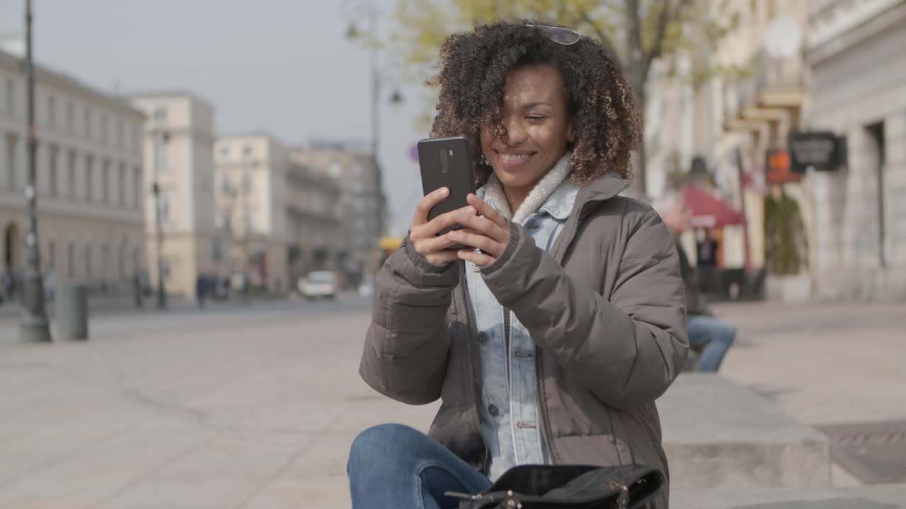 bella chica con corte de pelo afro sentada en un banco en la calle de la ciudad