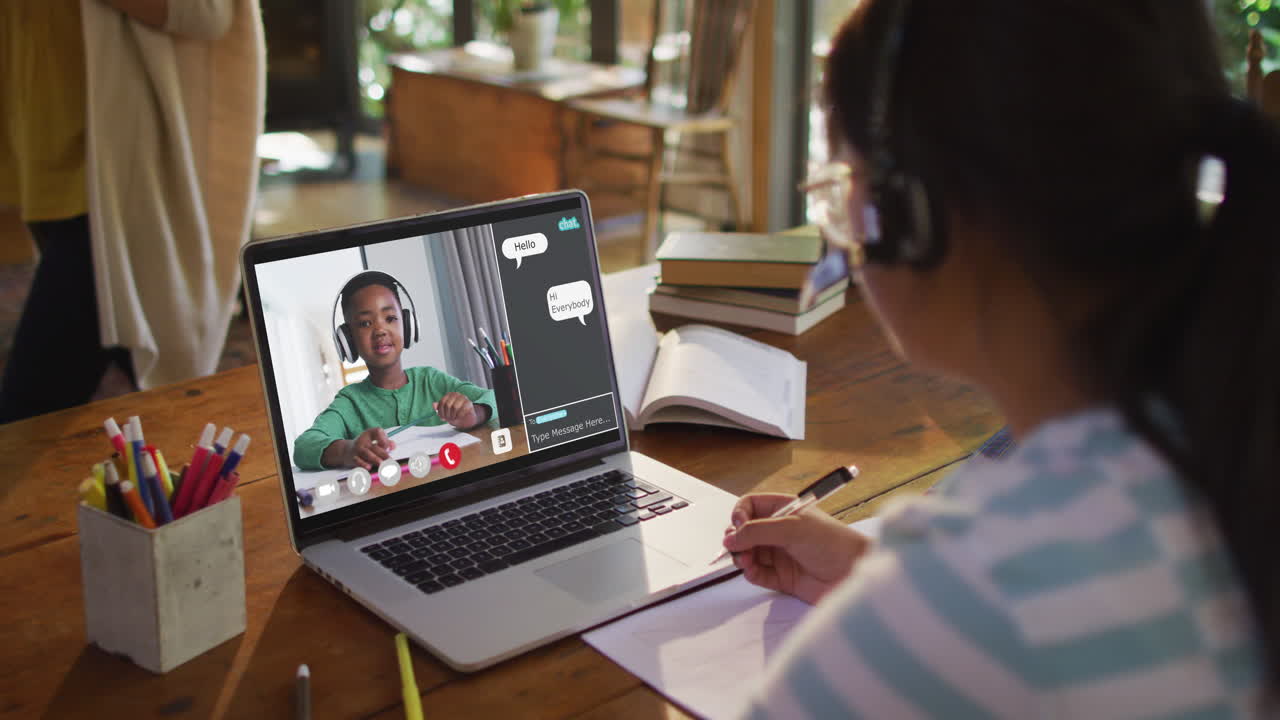 African american girl doing homework and having a video call with classmate on laptop at home