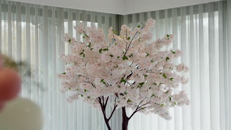 soft pink artificial cherry blossom tree brightens a white curtain backdrop in indoor space