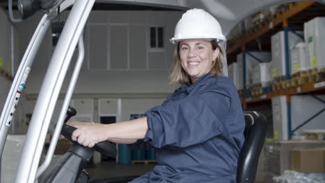 happy caucasian female worker sitting in forkfit and looking at the camera