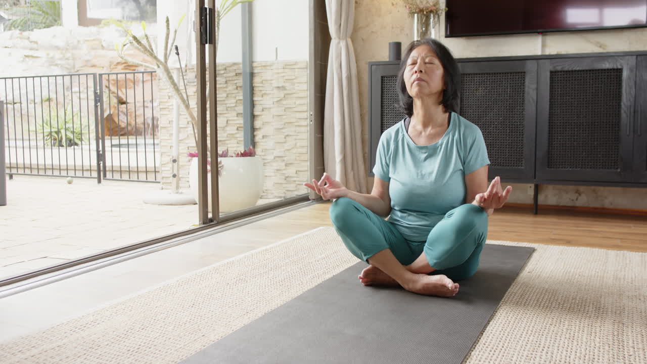 Senior woman meditating on yoga mat at home, finding peace and relaxation, copy space