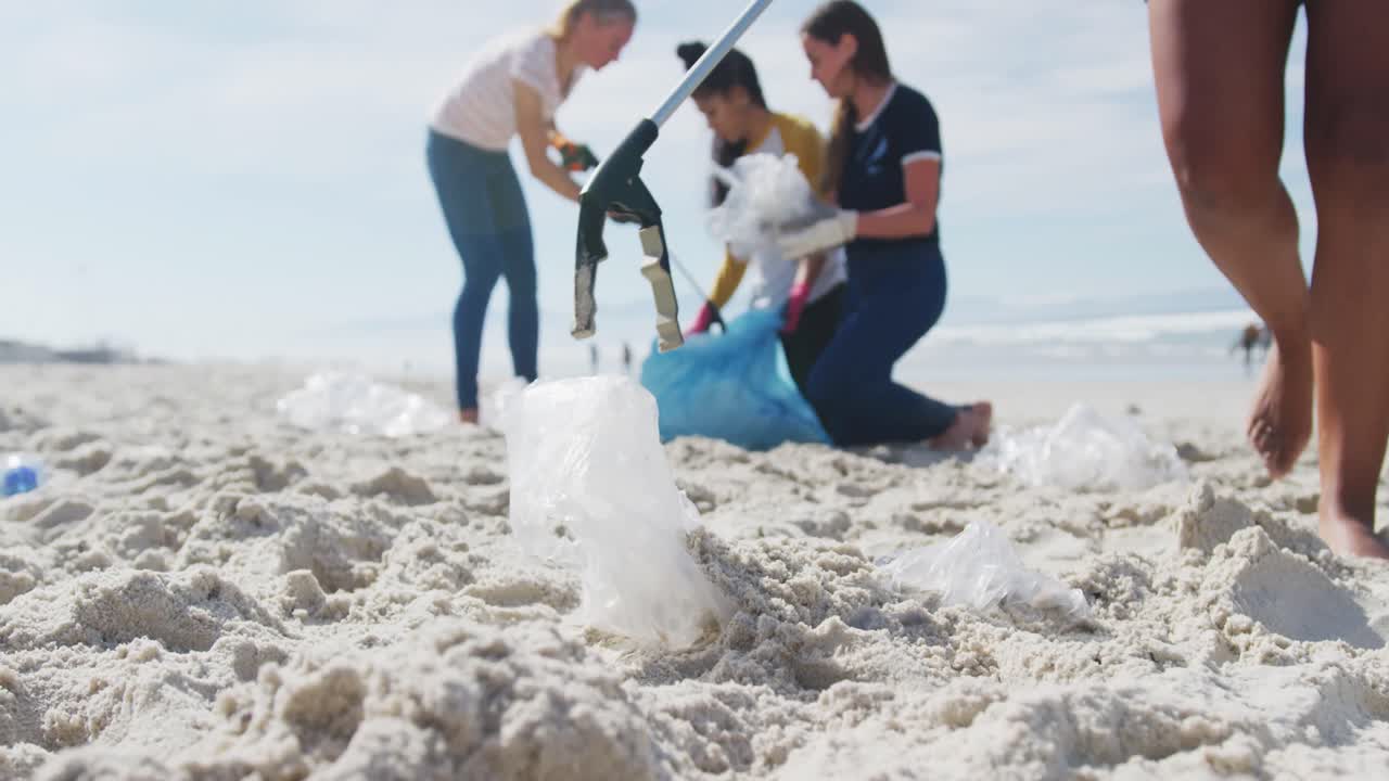 다양한 여성 친구 들 이 해변 에서 쓰레기 가방 에 쓰레기 를 넣고 있다