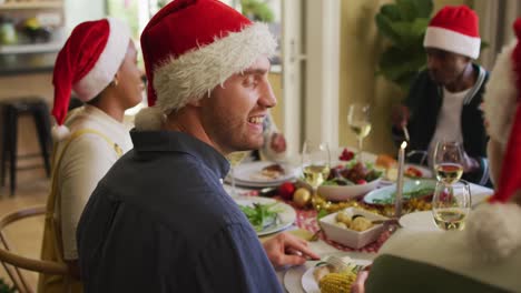 feliz hombre caucásico en sombrero de santa celebrando la comida con amigos en tiempo de navidad