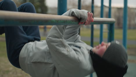 close-up of a young boy exercising on an iron bar in the stadium, he is wearing a gray jacket and beanie
