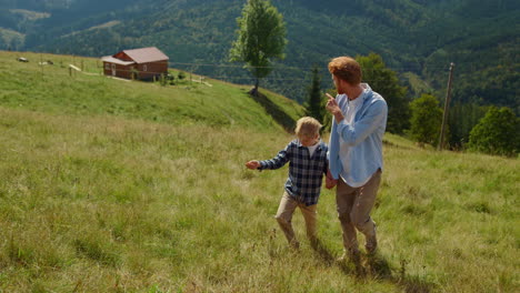 Father-son-enjoy-walk-on-green-hill.-Man-showing-mountain-views-to-boy-sunny-day