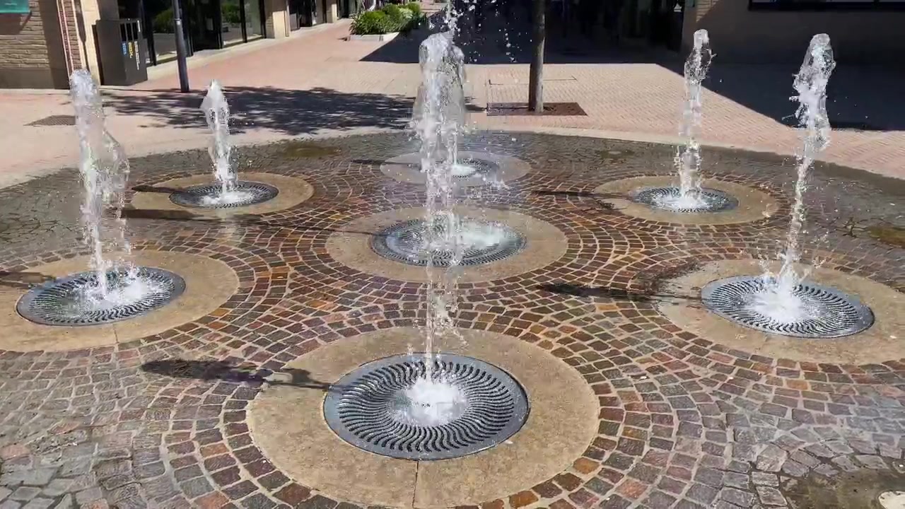 Fuentes de agua danzantes modernas en una soleada plaza de un centro comercial outlet. 4K