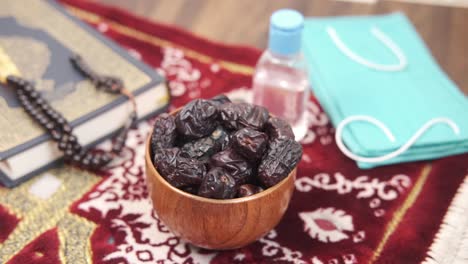 holy book quran, date fruit , mask, hand sanitizer and prayer beads on floor